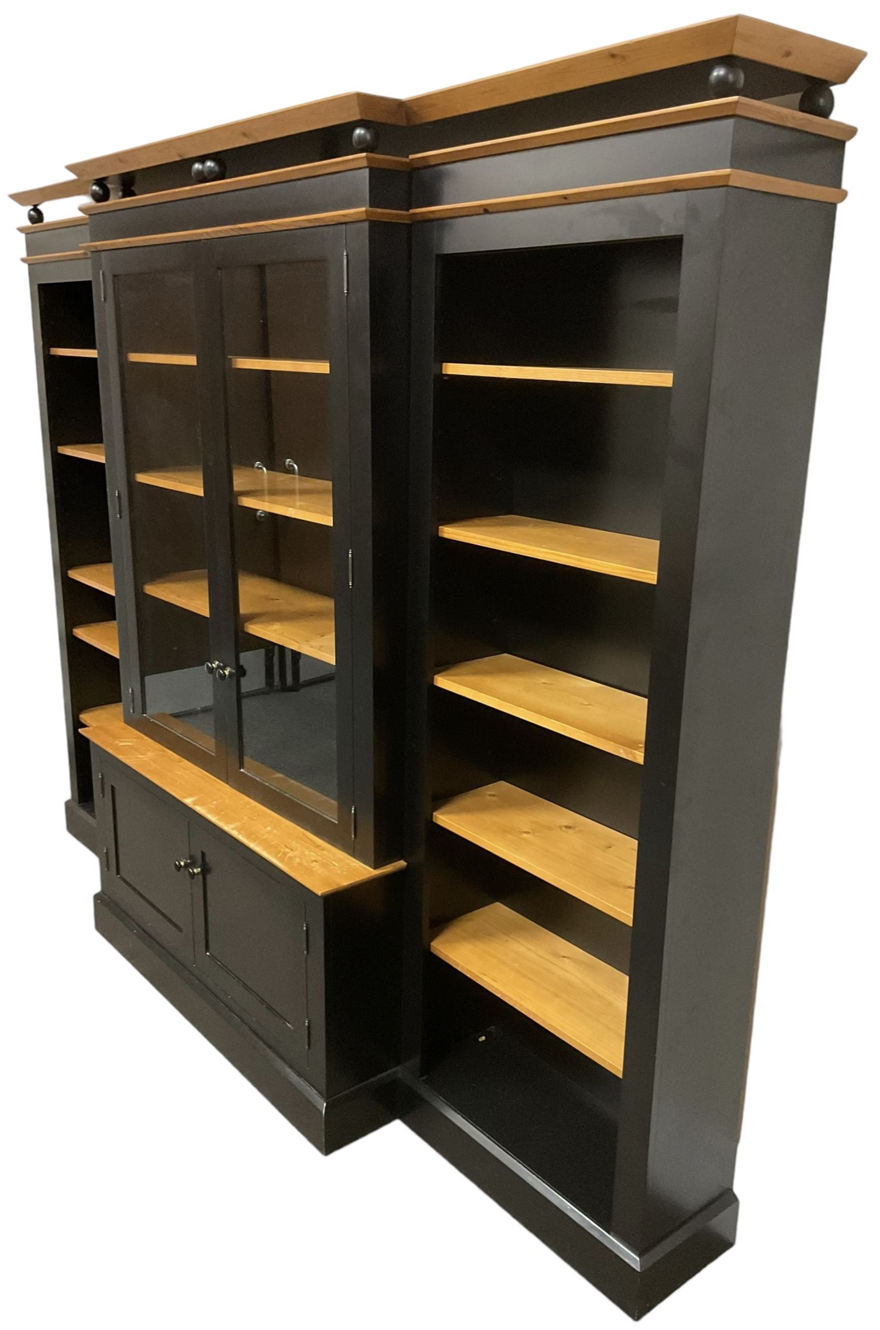 Contemporary polished pine and black finish break-front bookcase, projecting cornice over globular mounts, central cabinet enclosed by two glazed doors over double panelled cupboard, flanked by adjustable shelves, on plinth base