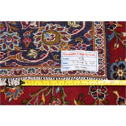 Central Persian Kashan hand-knotted carpet, crimson ground field, with central cusped lozenge medallion, enclosing a palmette and a floral rosette arrangement, surrounding field densely populated with scrolling arabesques, flowering vinery and stylized boteh motifs in tones of indigo, pale blue, ivory and ochre and spandrels of confirming design, flanked by multiple guard stripes, with cotton fringe ends 