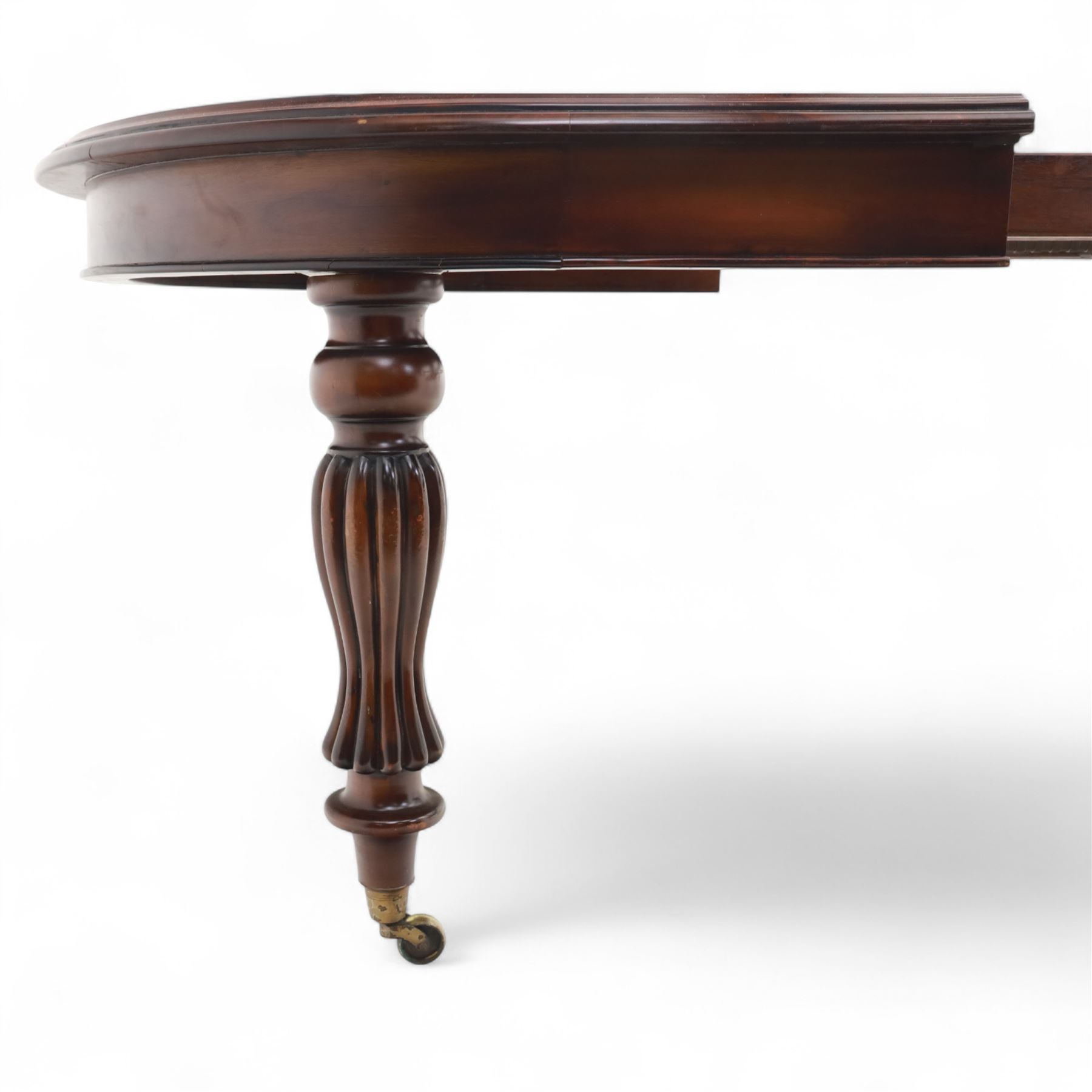 Victorian mahogany extending dining table, rounded rectangular top with moulded edge, pull-out action fitted with two additional leaves, raised on four reeded and fluted baluster legs with brass caps and castors