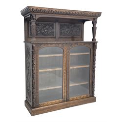 Victorian heavily carved oak buffet cabinet, projecting and gardroon carved canopy top over panelled back carved with grapes and vine, two tapering front supports with mask mounts, the rectangular top with foliate carved edge over two glazed doors, fitted with three adjustable shelves, the uprights carved with leaves and berries, plinth base