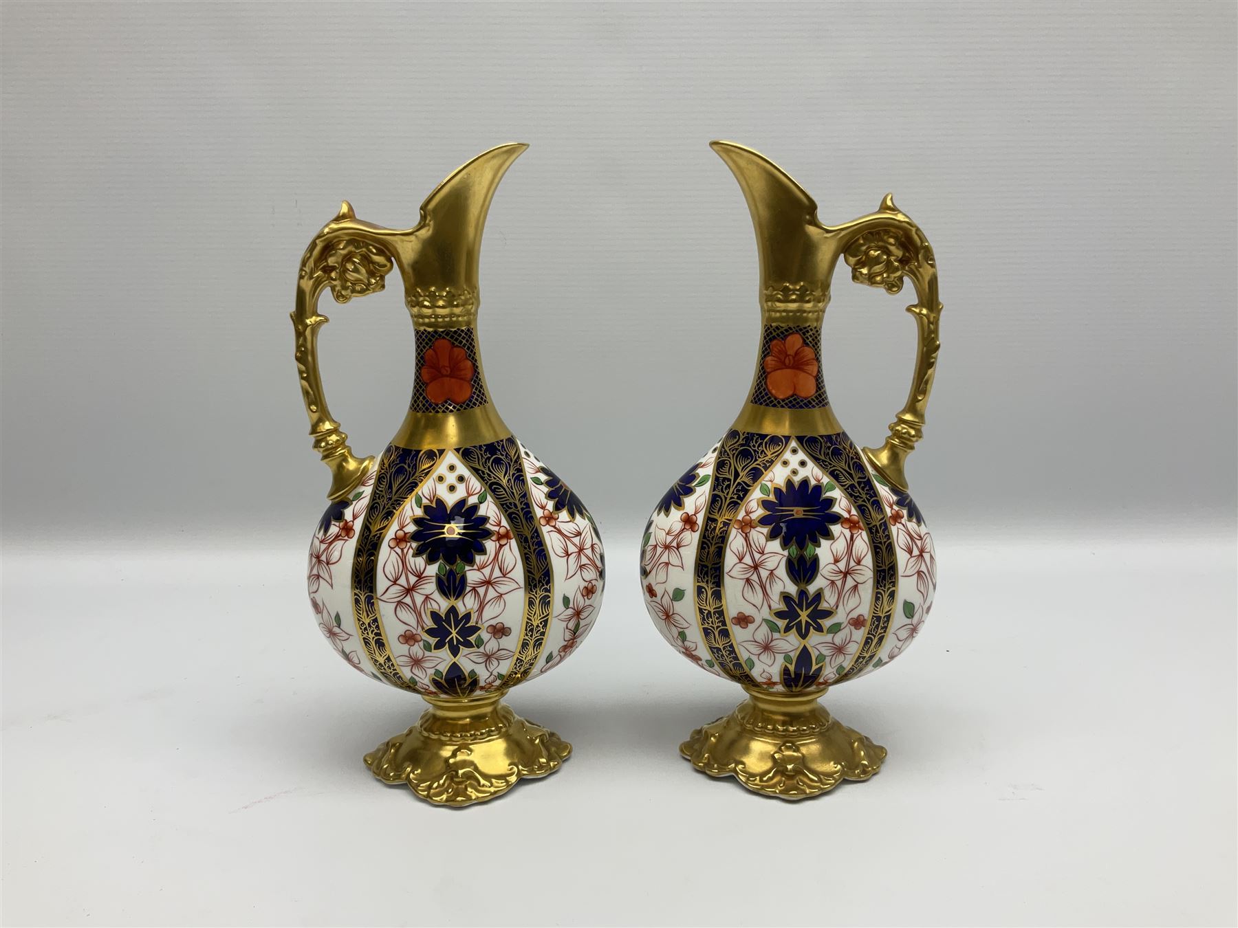 Pair of mid 20th century Royal Crown Derby Imari 1128 pattern Kedleston ewers, each with gilt scroll handle and neck, upon a gilt quatrefoil foot, each with printed marks beneath, H25.5cm