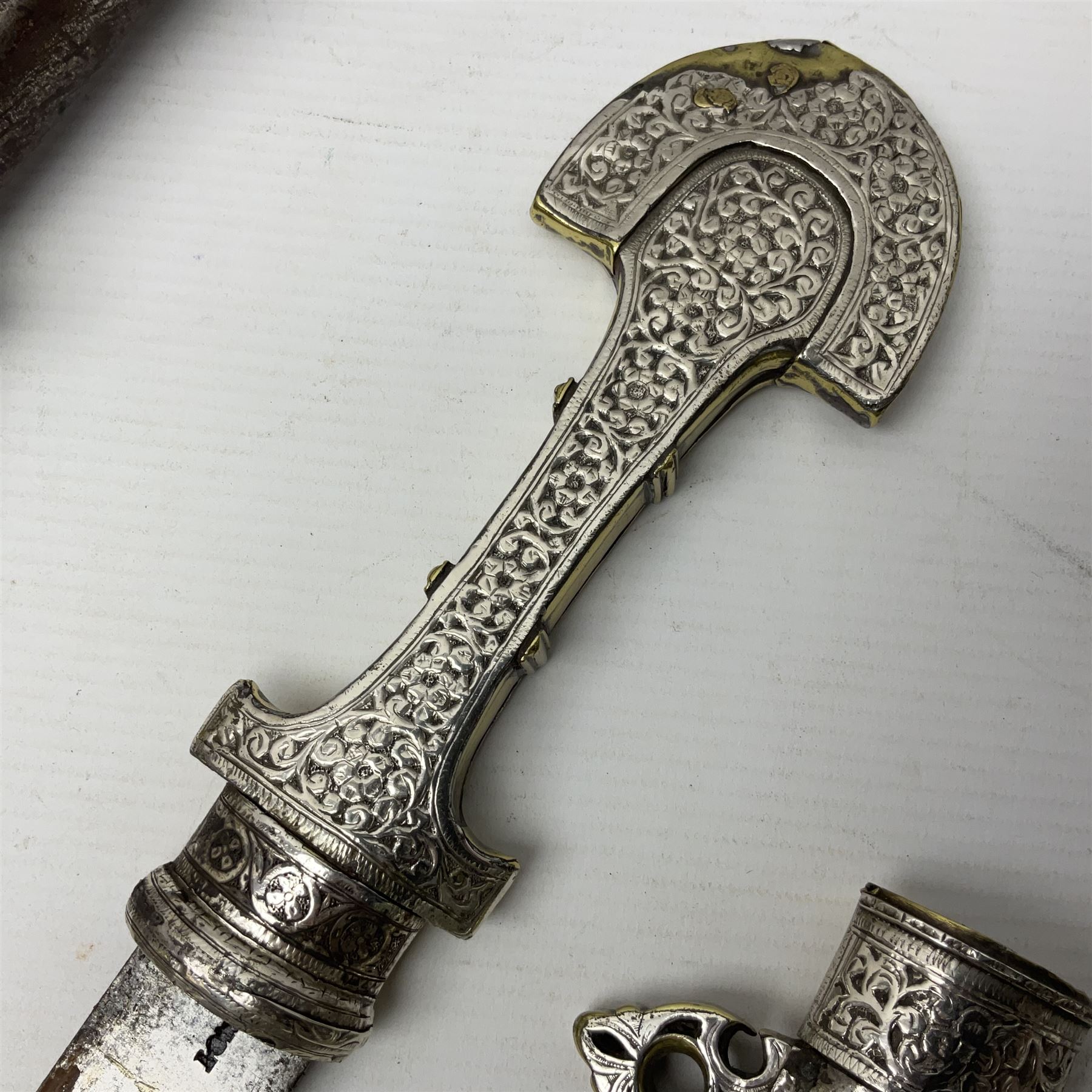 Moroccan jambiya dagger with 24.5cm plain curved blade stamped LONDON to the ricasso area, the hilt and scabbard overlaid with plain sheet brass to the back and ornate silver coloured metal to the front; waisted grip and arched pommel; two pyramid mounts to the scabbard L41cm overall; large billhook with curving blade and stacked leather washer grip; and a reproduction halberd blade (3)