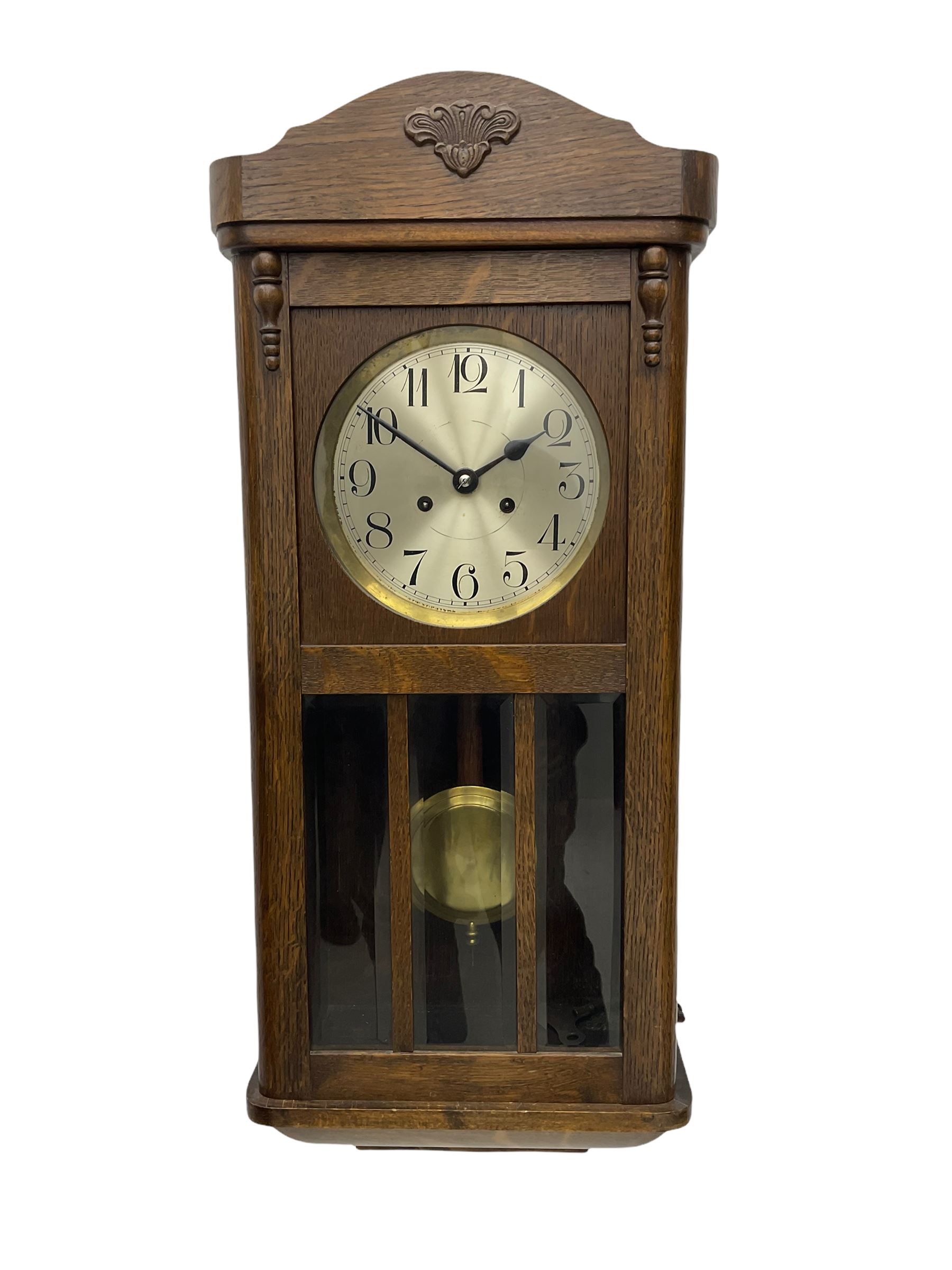 A 1930's wall clock in an oak case with a full-length door, three glazed panels and visible pendulum, case with a shaped pediment and applied carving, 6'' silvered dial with Arabic numerals, minute track and steel baton hands, eight day going barrel movement striking the hours on a gong.

	



