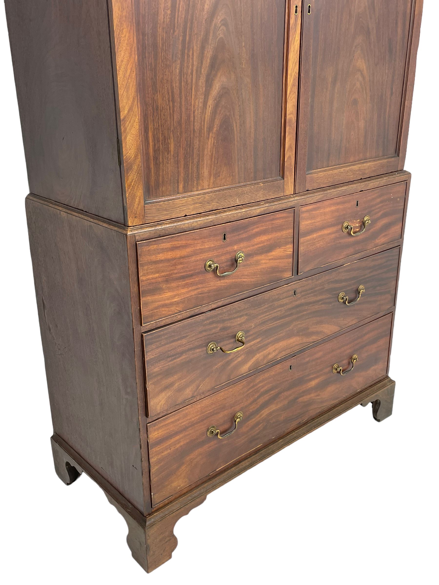 George III mahogany Gentleman's linen press, the projecting cornice over two panelled cupboard doors enclosing three sliding trays, the base fitted with two short over three long graduating cock-beaded drawers, lower moulded edge over bracket feet