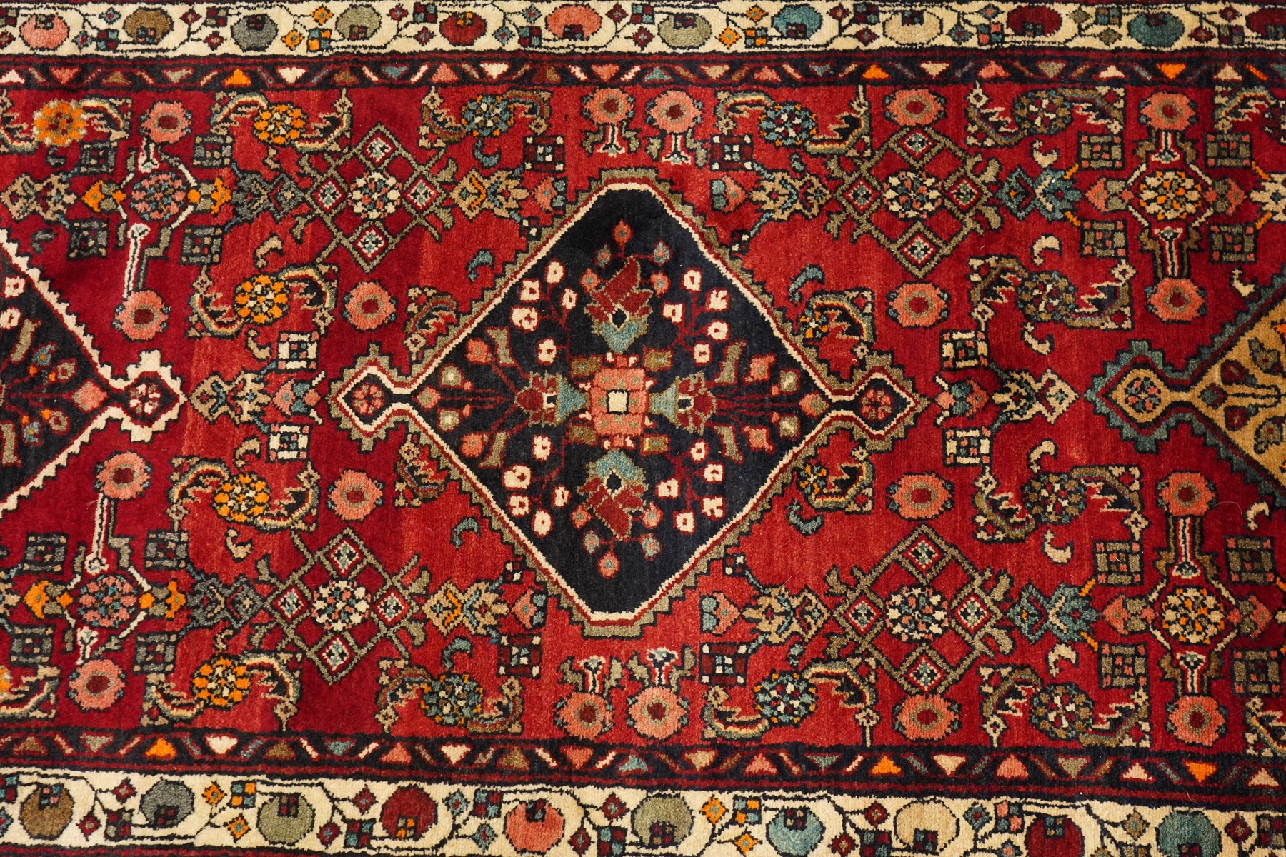 Large Persian Qashqai runner rug, the red ground decorated with navy and ivory lozenge medallions interspersed with stylised floral and geometric motifs, enclosed by an ivory flowerhead border and patterned guard stripes