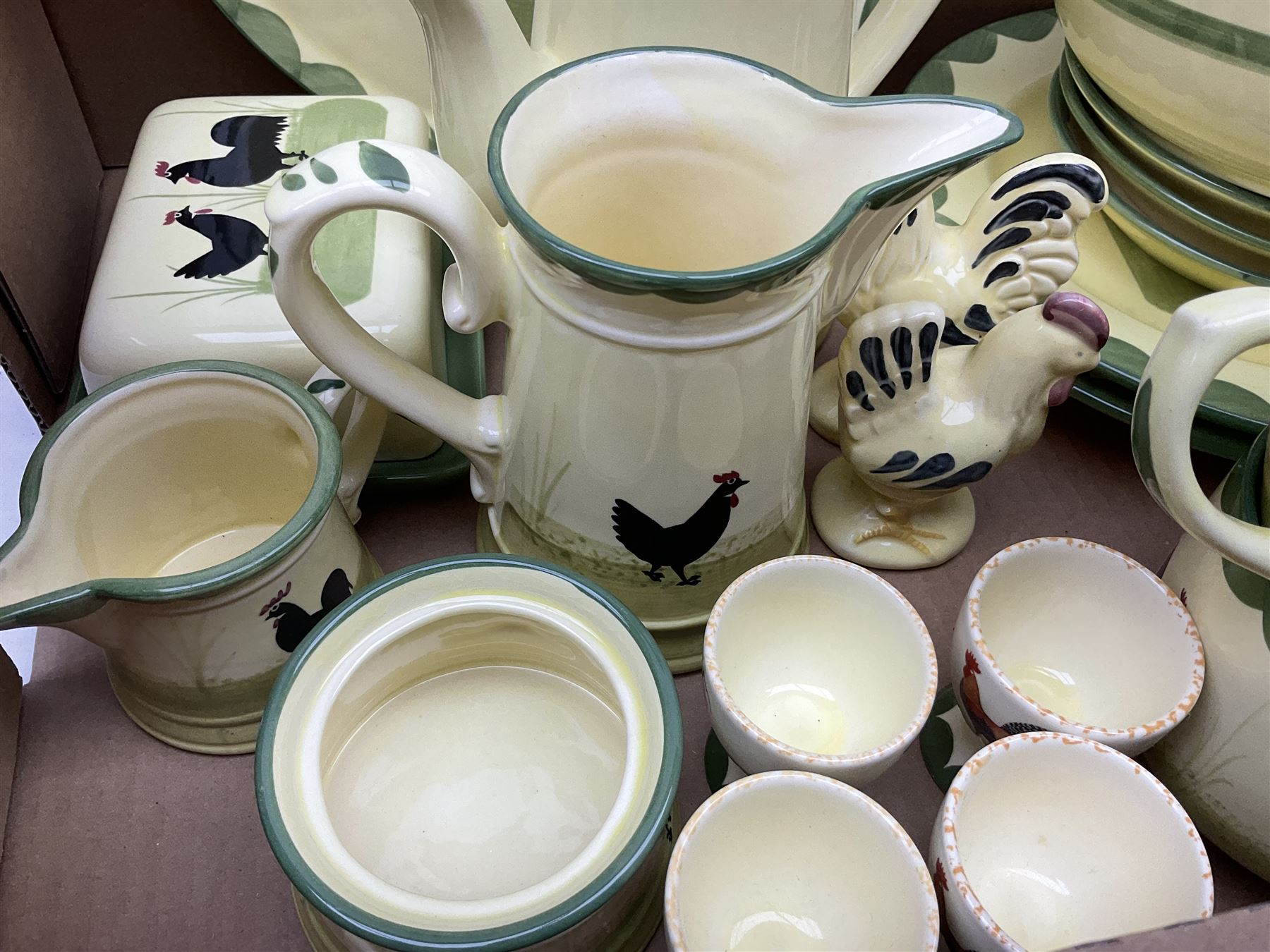 Zeller Fayencerie dinner and tea wares, decorated in cockerels against a yellow ground, with green scalloped border, comprising cake stand, two plates, bowl, three large teacups and saucers, coffee pot, milk jug, cream jug, lidded sugar bowl, pair of cruets modelled as cockerels, butter dish and cover, and utensils pot, and four similar egg cups, in one box 