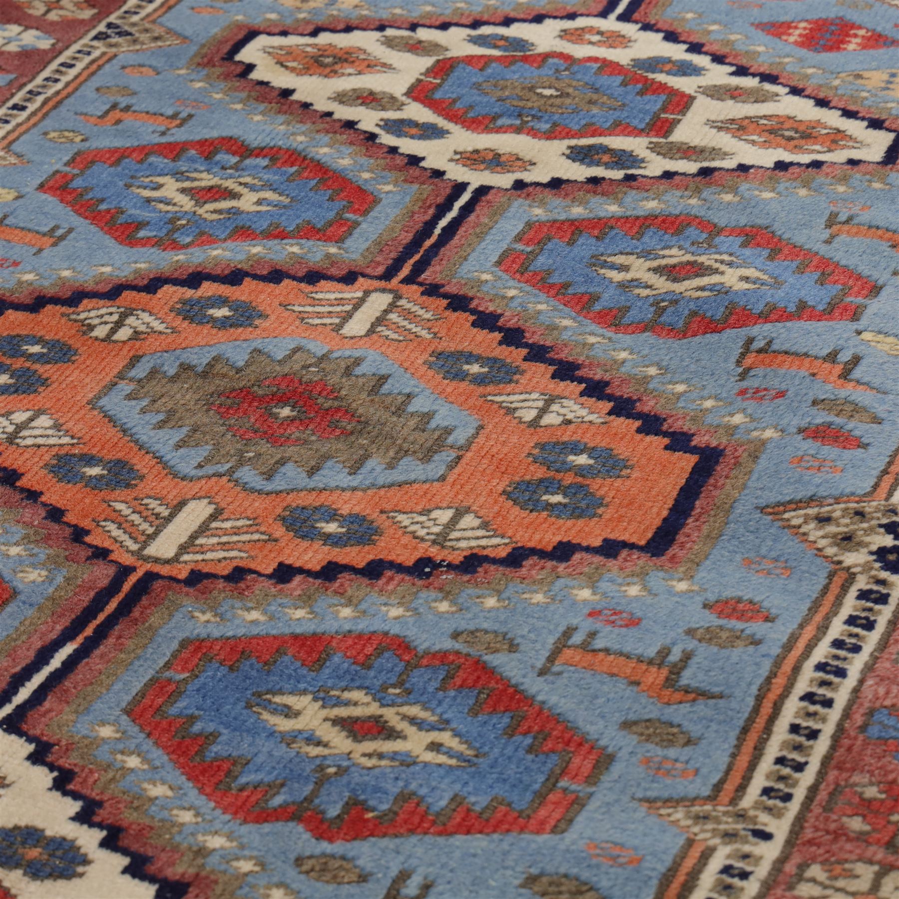 Caucasian Kazak hand-knotted rug, pale blue main field with large geometric medallions in a vertical arrangement and angular tribal motifs within a rosette and geometric border, cotton fringe end, 68x88cm