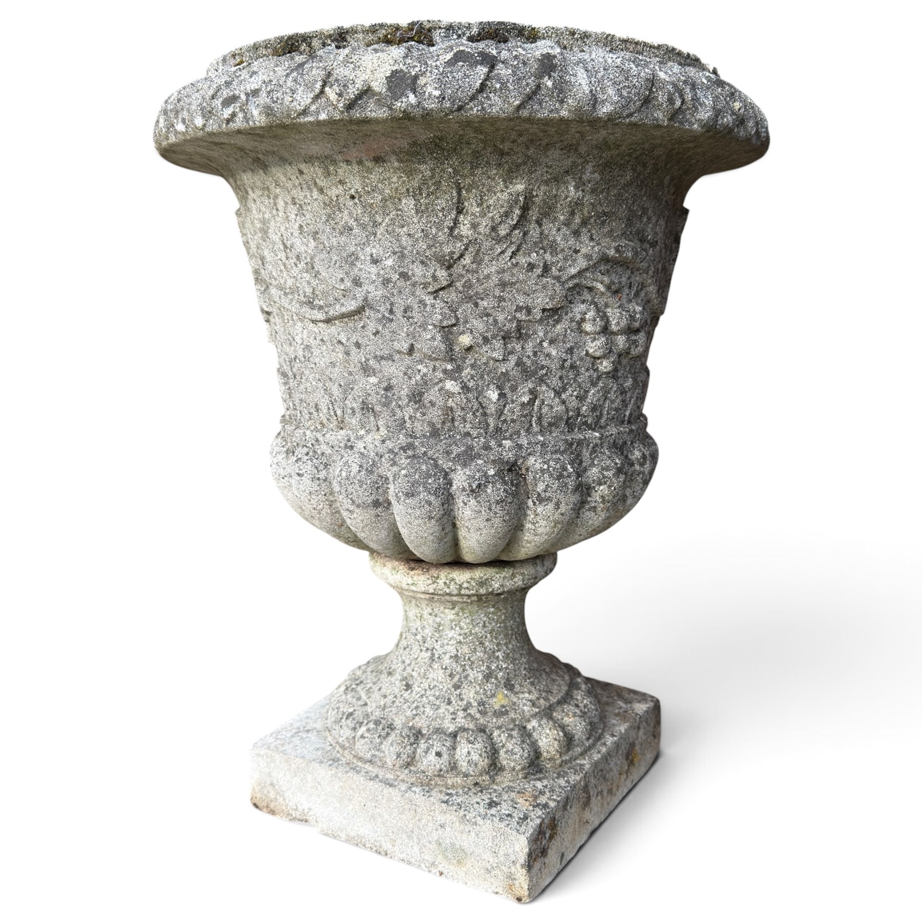 Set of four weathered composite stone urns of campana form, the everted leaf-moulded rolled rim over a body decorated with scrolling fruiting grapevines in relief, over a gadrooned underbelly and waisted socle, lobed collar on square base