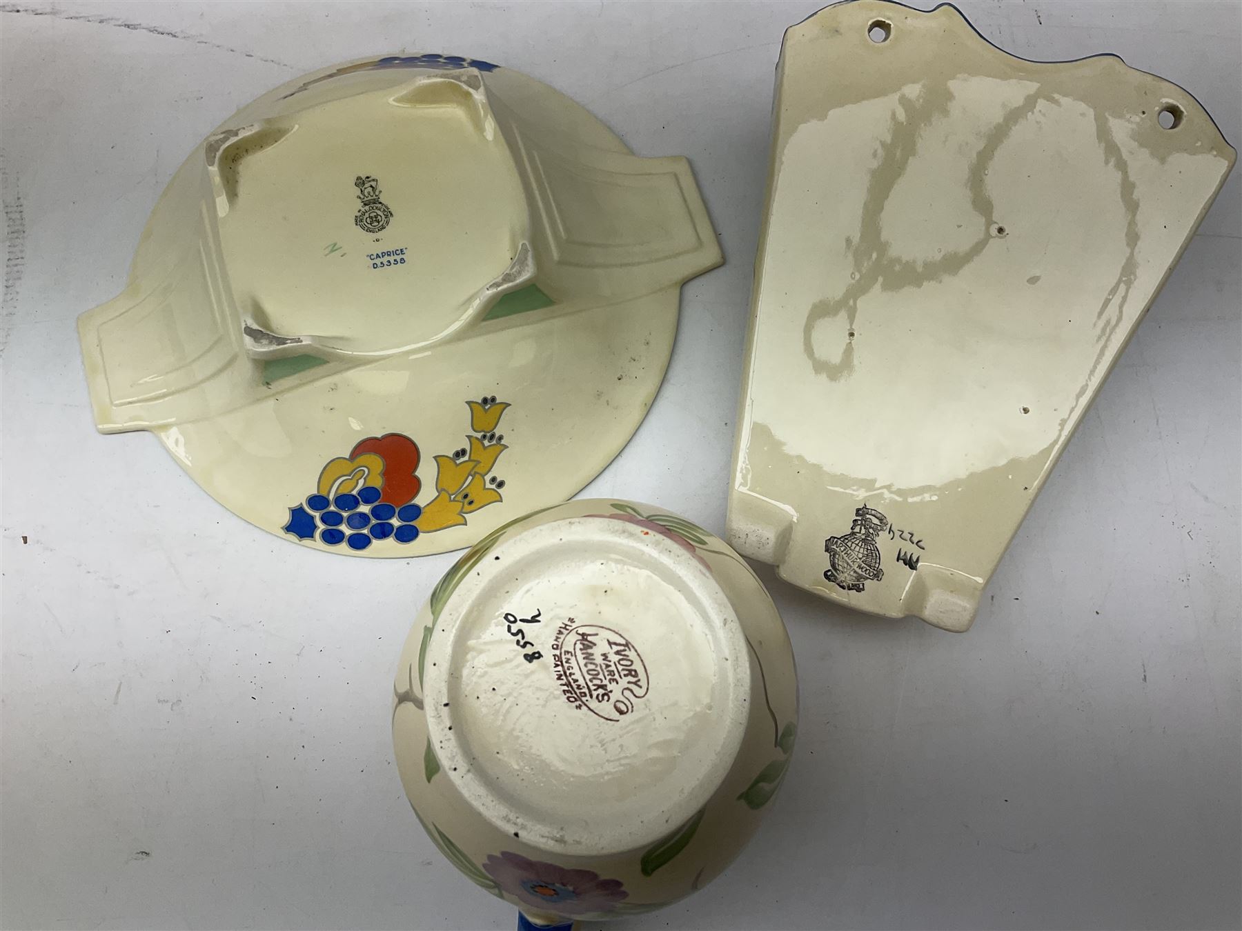 Group of Art Deco ceramics, comprising Wadeheath jug painted in spiralled bands of blue, orange, yellow and brown, shape no. 707784, Royal Doulton Caprice pattern twin handled bowl, no. D5358, Arthur Wood wall pocket of typical stylised fan form with painted floral decoration, Arthur Wood vase of cornucopia form with red and grey floral decoration, Wadeheath jug of ribbed form with stylised handle, and two Hancock's Ivory Ware jugs, tallest example H26cm