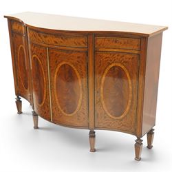 Quality handmade Sheraton Revival inlaid mahogany serpentine-front commode sideboard, shaped rectangular top with boxwood stringing, the banded frieze fitted with three drawers, over four matched-veneer cupboards with oval inlays and banding, raised on square tapering and turned feet with gadroon carving, retailed by David Hick Interiors, Jersey