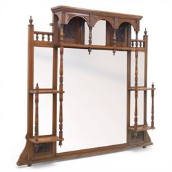 Edwardian walnut overmantel mirror, moulded cornice over three arched apertures with turned supports, flanked by open shelves with turned uprights and finials, carved foliate panels to the base