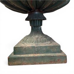 Pair of Victorian cast iron campana garden urns, the flared rim with repeating stylised anthemion motifs with scrollwork, over a deep gadrooned and Aesthetic moulded underbelly, fluted and foliate lower bowls on square pedestal bases, in antique green-painted finish
