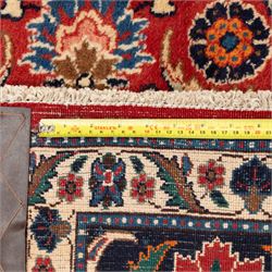 North West Persian carpet, the red field decorated with an all over repeating design of palmettes, rosettes and curling serrated leaves in indigo, ivory and ochre tones, enclosed by an indigo scrolling floral border and ivory flowerhead guard bands