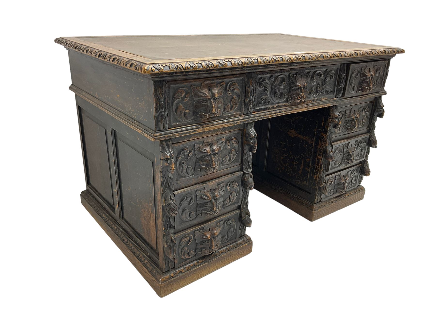 Late 19th century Gothic revival carved oak twin pedestal desk, rectangular top with inset writing surface and carved edges, central frieze drawer flanked by eight drawers, all with green man carved handles and extending trailing foliage, carvings of pineapple and lion mask corbels, the pedestals with panelled sides and back, on plinth bases