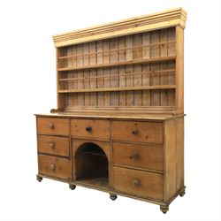 Early 19th century waxed pine farmhouse dresser and rack, the rack featuring two plate shelves and bars above seven drawer base with centre 'dog kennel' recess, raised on turned feet