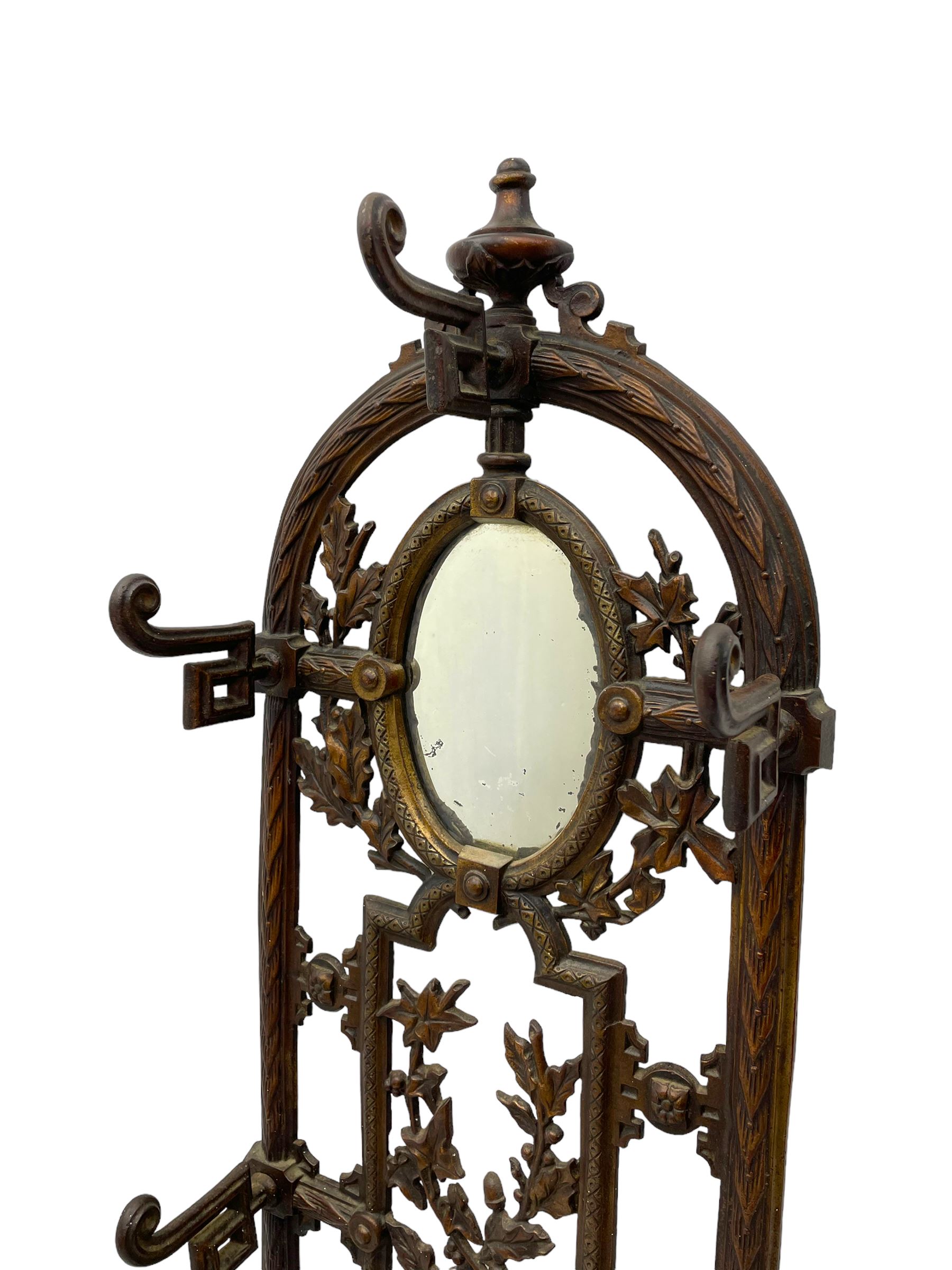 19th century cast iron hallway hat and coat stand, the arched frame decorated with overlapping foliage, central oval mirror surrounded by trailing oak leaves and acorns, with extending umbrella and stick stand, the curved plinth base decorated with acanthus leaves, with impressed and mounted R.d. lozenges