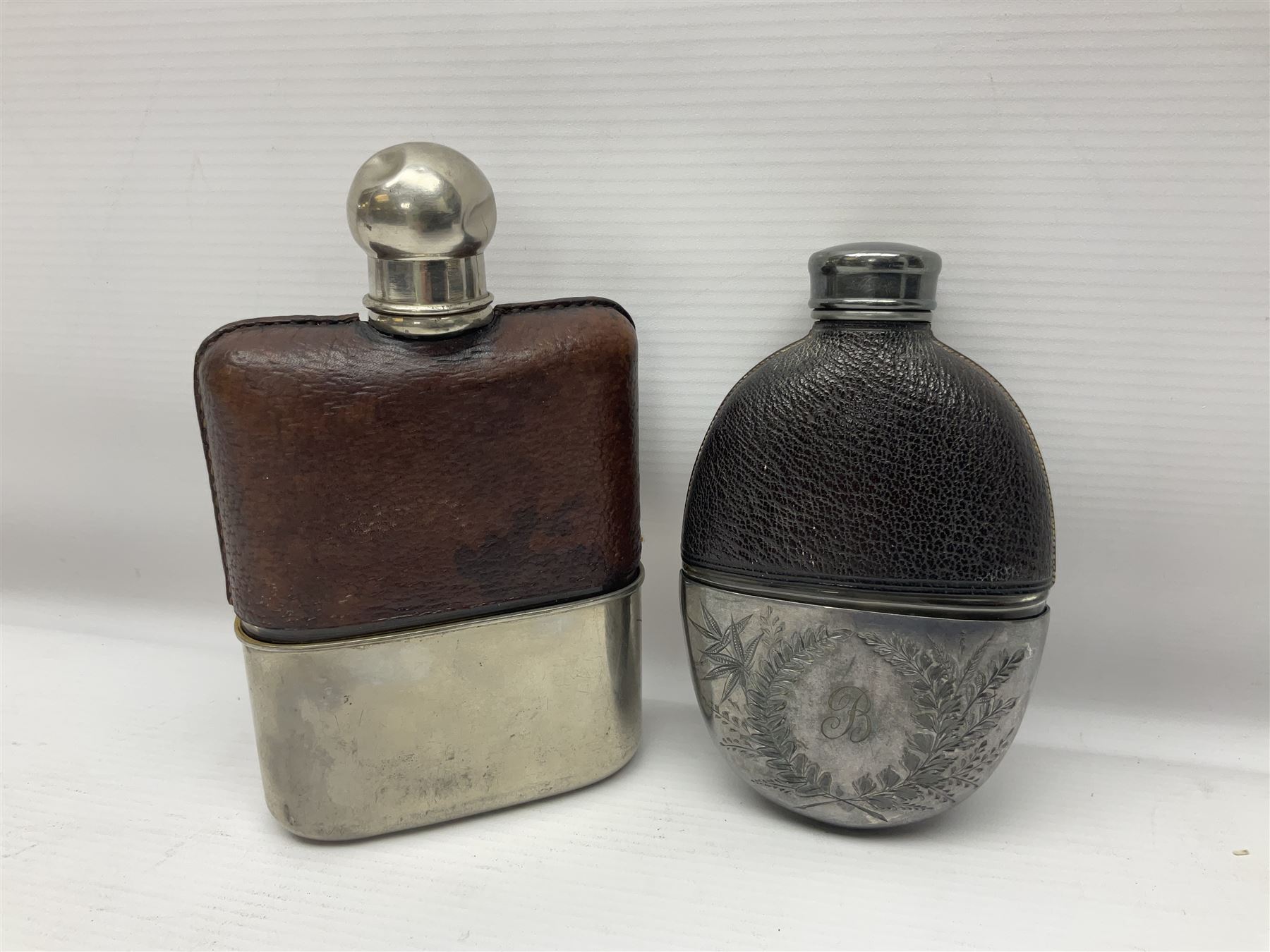Silver plated glass and pressed leather hip flask, with swivel cap and removable cup, together with a similar oval example, engraved with wreath and initial B, tallest H16.5cm