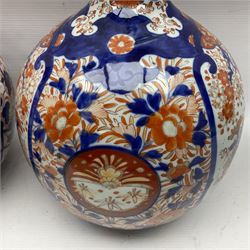 Pair of large 19th century Japanese Imari porcelain bottle vases, painted with shaped reserves of peonies, chrysanthemums and prunus blossom, each H46cm