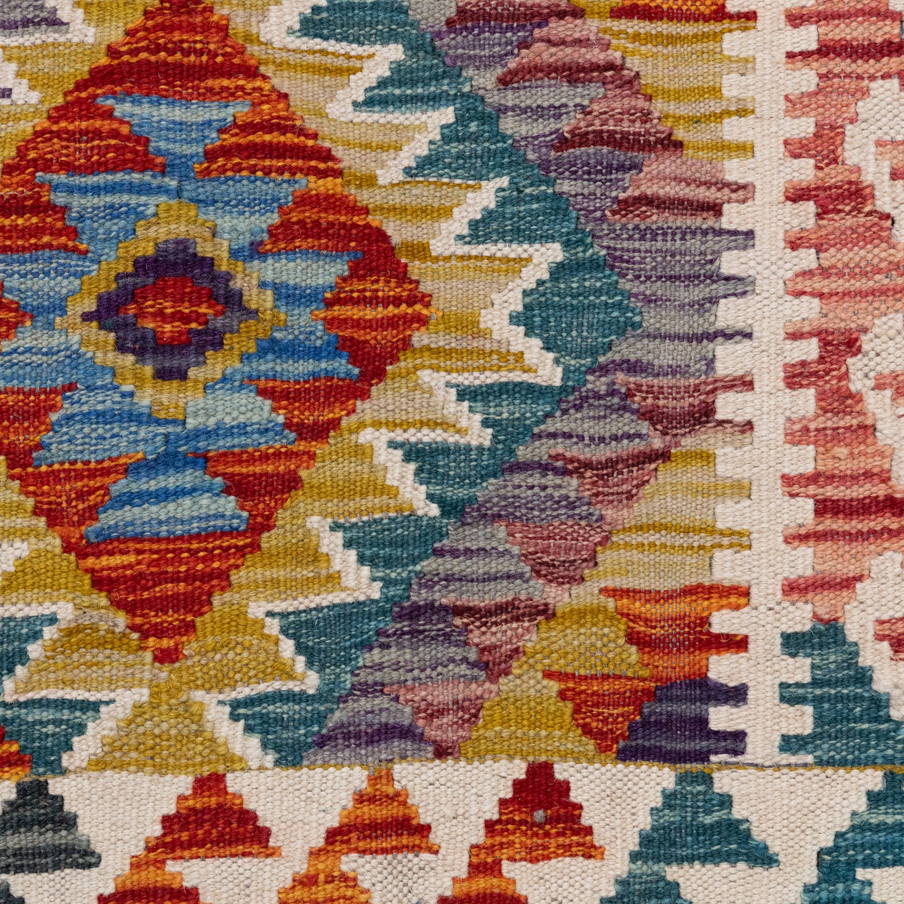 Afghan kilim multicoloured rug, the geometric field decorated with repeating lozenges of contrasting tones heightened with ivory outlines, the outer guard band with repeating hooks and Vitruvian scrolls