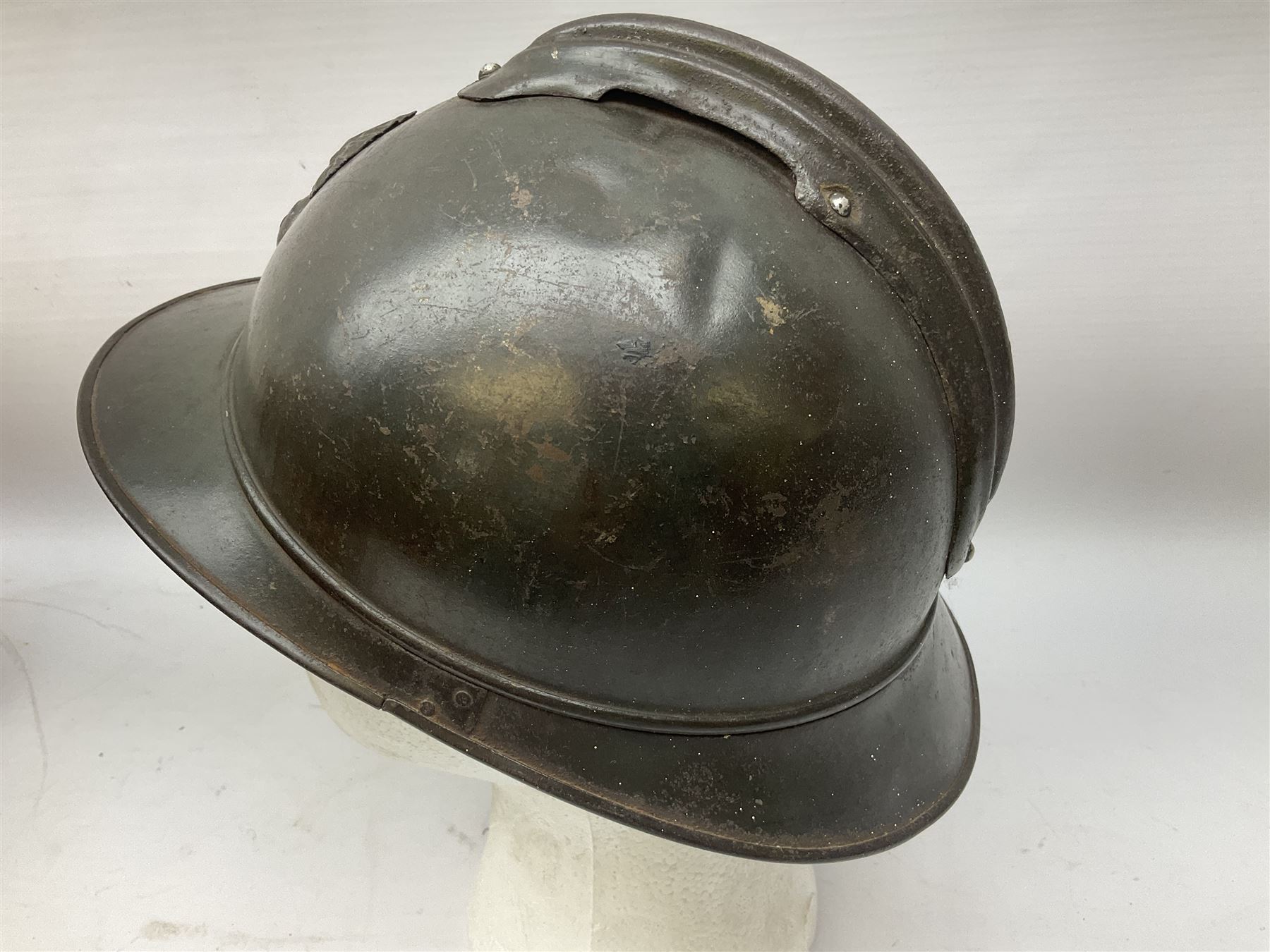 WW2 French M-26 Adrian Pattern Steel Helmet, original olive drab paint finish; flaming grenade badge to the front signifying issue to an Infantry regiment; original leather liner and leather chinstrap; and WW2 Dutch steel helmet with liner and chin strap (2)