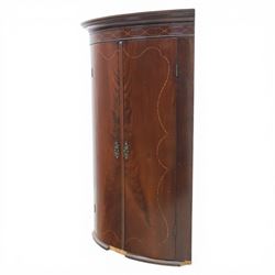 George III mahogany bow-front corner cupboard, projecting moulded cornice over satinwood inlaid frieze with geometric crossbanding, enclosed by twin shaped panel doors with line inlay and ornate brass escutcheon plates, painted interior fitted with shaped shelves, on moulded plinth base