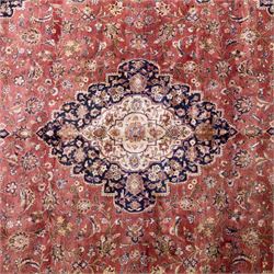 Large Central Persian Kashan hand-knotted carpet, madder red field with central cusped medallion on beige ground enclosed by indigo border with an intricate all-over arrangement of scrolling vines and floral motifs within conforming spandrels and a indigo ground main border ornamented with floral designs, enclosed by guard stripes and cotton fringe ends 