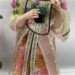 Anna Meszaros Hungary - three hand made needlework figurines - 'The Cobbler' as a child seated in a wooden rocking chair working on a removed boot H28cm; young girl in a long floral dress standing playing a harp H35cm; and young girl wearing a blue tabard standing playing a lute (3) Auctioneer's Note: Anna Meszaros came to England from her native Hungary in 1959 to marry an English businessman she met while demonstrating her art at the 1958 Brussels Exhibition. Shortly before she left for England she was awarded the title of Folk Artist Master by the Hungarian Government. Anna was a gifted painter of mainly portraits and sculptress before starting to make her figurines which are completely hand made and unique, each with a character and expression of its own. The hands, feet and face are sculptured by layering the material and pulling the features into place with needle and thread. She died in Hull in 1998.  