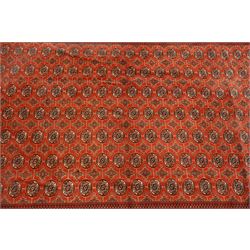Turkmen hand-knotted carpet, madder red field, with an all-over design of row of Tekke guls, each enclosing stylized cruciform and geometric devices in tones of ivory, dark brown, and indigo, principal border of stylized geometric motifs, flanked by guard border with angular latch hook geometric designs, with cotton fringe ends 