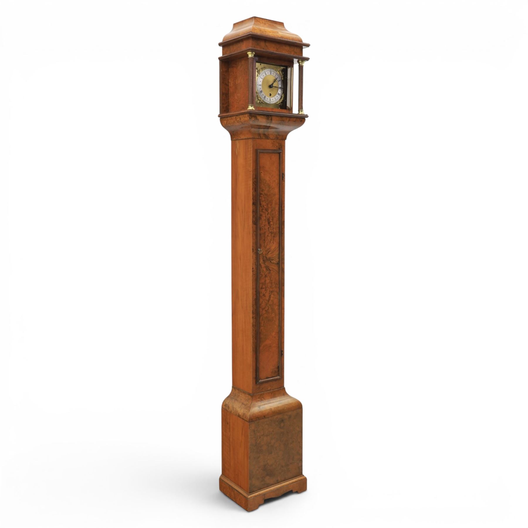 Early 20th century walnut small longcase clock, brass dial with silvered Roman numeral chapter ring and pierced black hands, the figured walnut case with shaped projecting hood, long moulded trunk door and stepped plinth base