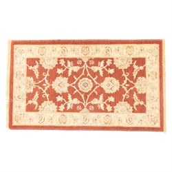 Lot of three Indo-Ziegler style wool rugs, comprising one with central floral medallion and palmette border, and two matching examples with scrolling vine and flowerhead motifs on a deep red field, each with decorative border in soft gold tones (60cm x 85cm) (65cm x 115cm)