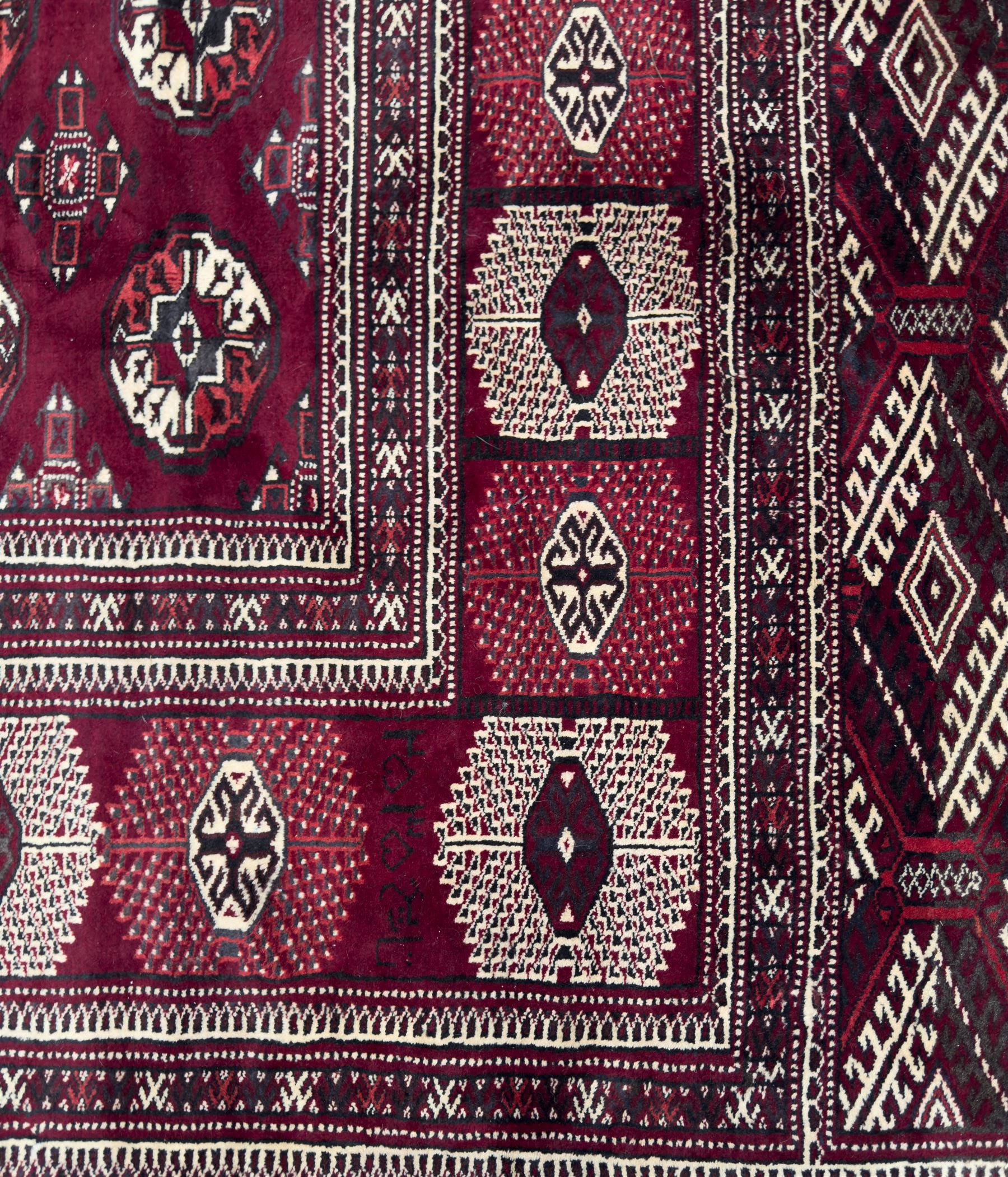 Northeastern Persian Yamut  hand-knotted carpet, the rich burgundy field with repeating rows of stepped gul motifs in cream and black, enclosed by multiple linear and geometric borders with hooked motifs and diamond medallions