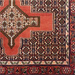 North West Persian Senneh hand-knotted runner, decorated with a continuous series of stepped and hooked geometric medallions against a madder red ground, enclosing herati style and small geometric floral motifs, framed by a principal border and flanked by multiple narrow guard stripes, with cotton fringe ends 