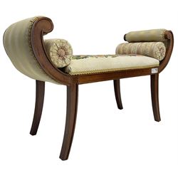 Regency design mahogany framed window seat, the scrolled arms upholstered in striped fabric, the stuffed seat in floral embroidered fabric, on sabre supports, with two bolster cushions