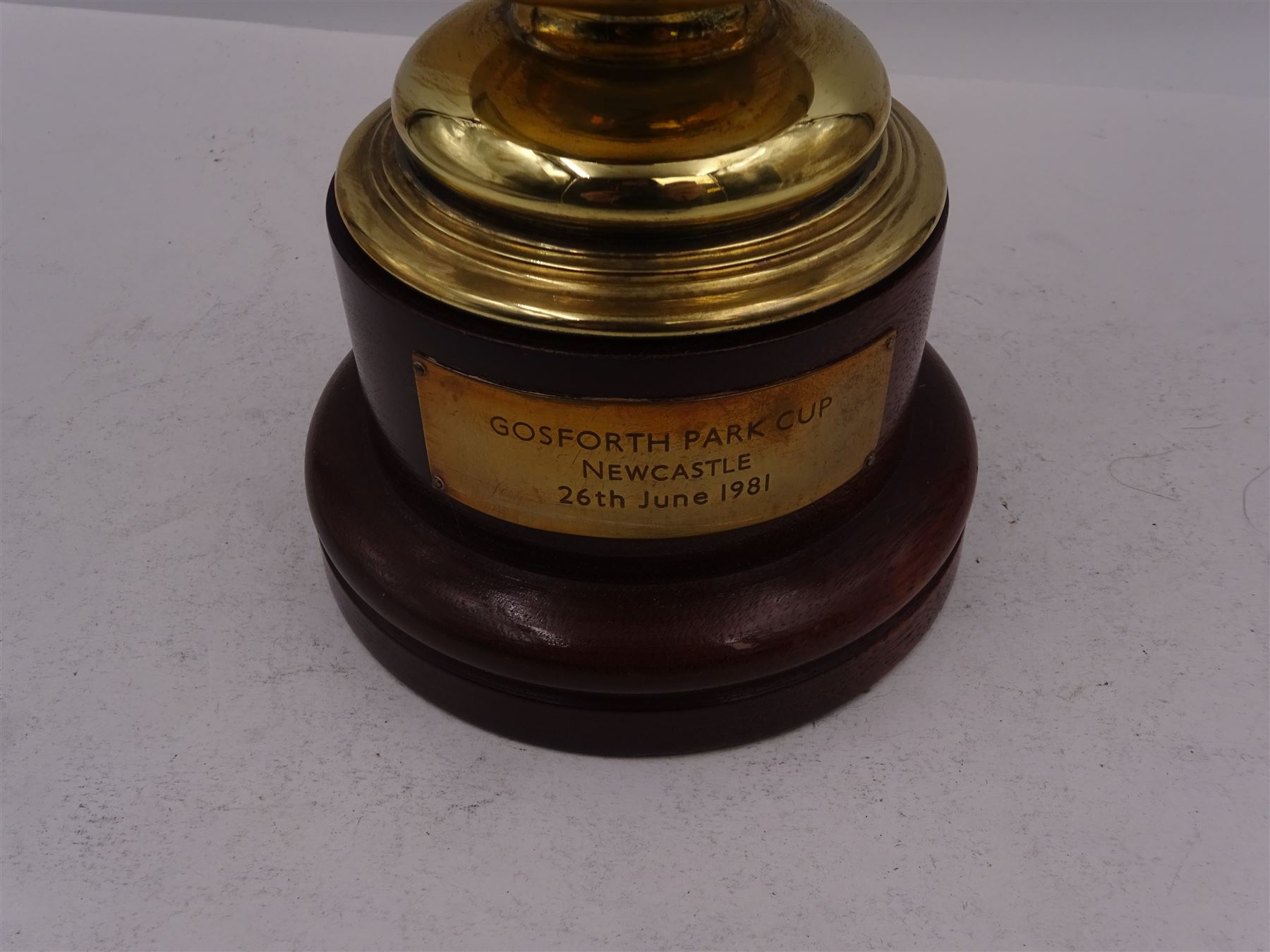 Edwardian silver-gilt twin handled trophy cup and cover, with two curved handles, the domed cover with urn finial, upon domed stepped foot and cylindrical mahogany base with applied plaque, hallmarked Skinner & Co, London 1908, total H29.7cm