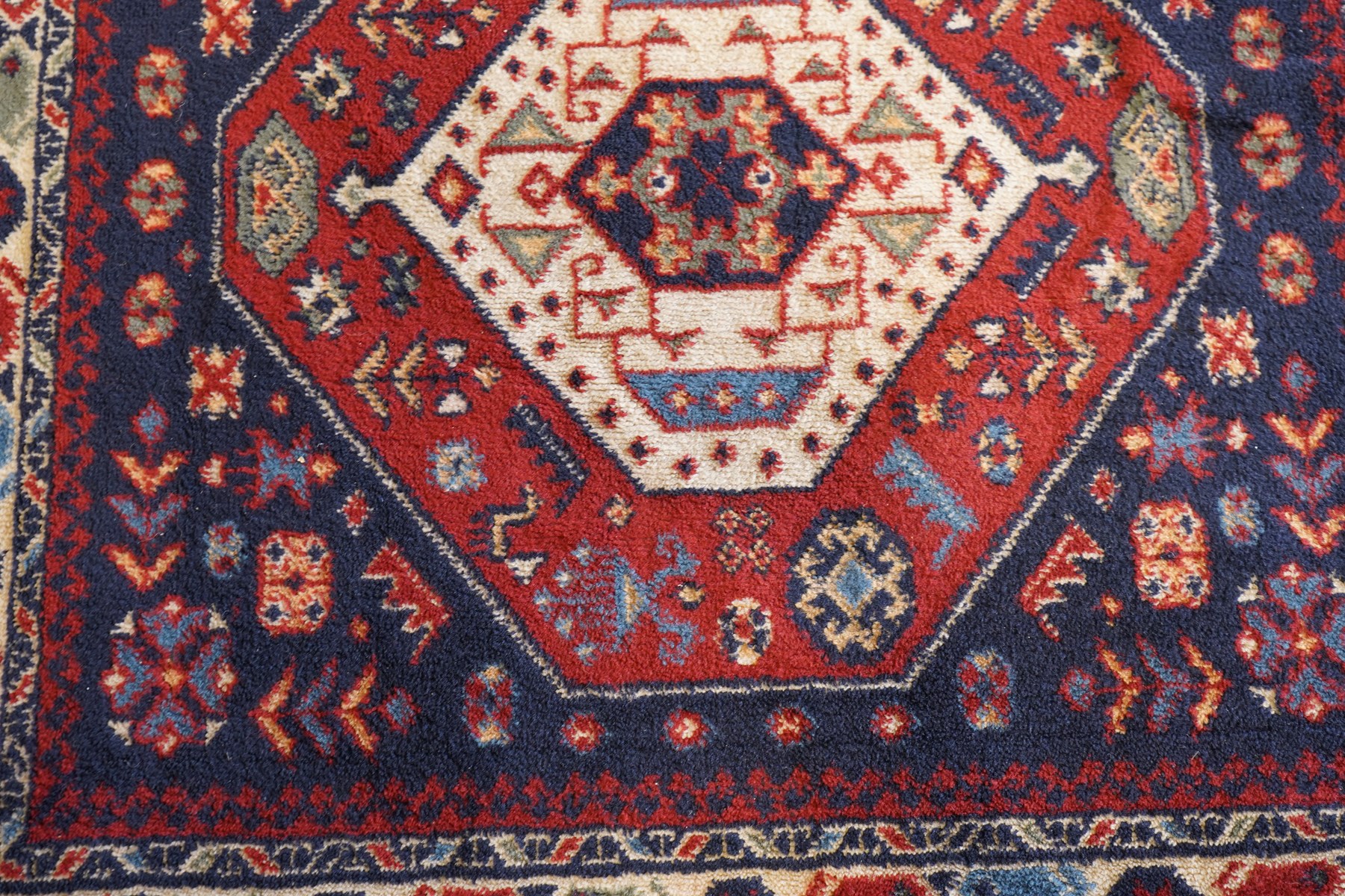 Four small Persian and Caucasian design rugs, comprising a Kazak rug with twin hooked medallions on a red ground, Baluchi rug with geometric motifs on a muted red ground, Shiraz rug with a central ivory and red medallion on a blue ground, and a Bokhara mat with four guls on a rose ground, each enclosed by geometric borders, largest 143cm x 88cm (4)