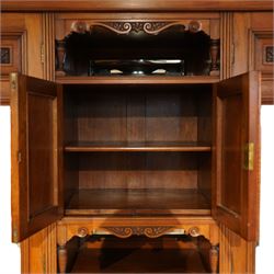 Edwardian walnut triple combination wardrobe, projecting pediment with pierced foliate scroll cresting above a central cupboard flanked by bevelled mirrored doors, the central section with twin panelled cupboard doors carved with foliate scrolls, over open recess with mirrored back and turned supports, above two short and three long drawers with brass handles, interior fitted with hanging rails and shelf, raised on plinth base
