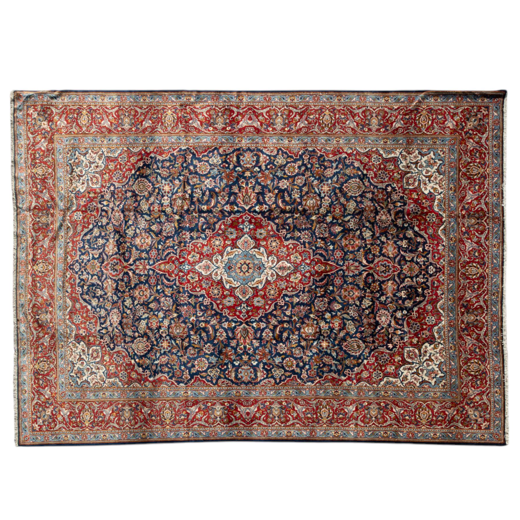 Persian Kashan carpet, navy field with central red diamond medallion enclosing floral rosette, framed by dense scrolling foliage and palmettes, triple borders in red, blue and ivory, originating from central Iran