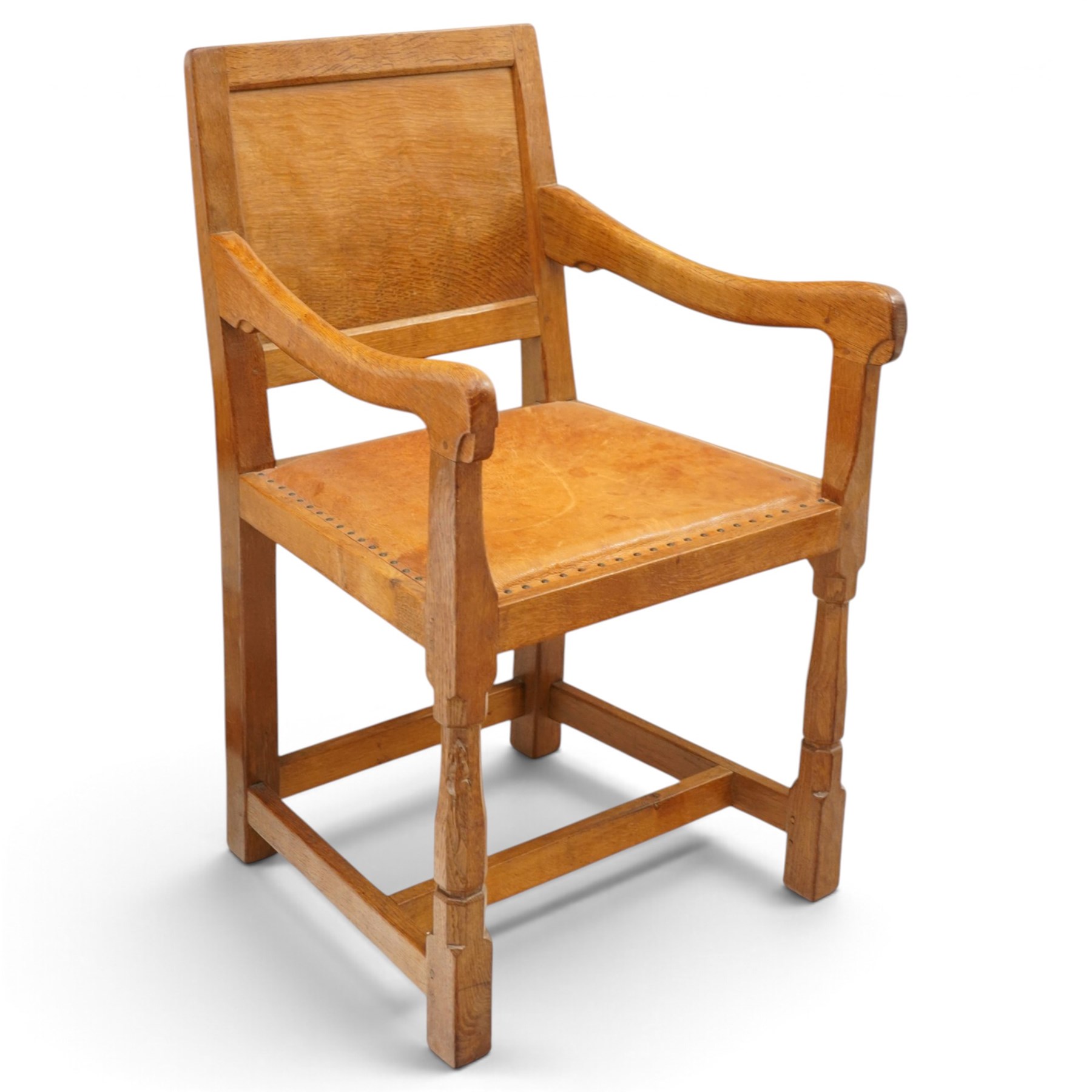 Mouseman - set of six (5+1) 1940s pre-war panel-back dining chairs, the raised backs with adzed panels, over seats upholstered in tan leather with studwork border, raised on octagonal turned baluster supports united by box stretcher, with carved mouse signature, by the workshop of Robert Thompson of Kilburn

Provenance: ordered directly from the Mouseman workshop in the 1940s before the outbreak of the war, the items were subsequently delivered after the end of war. 