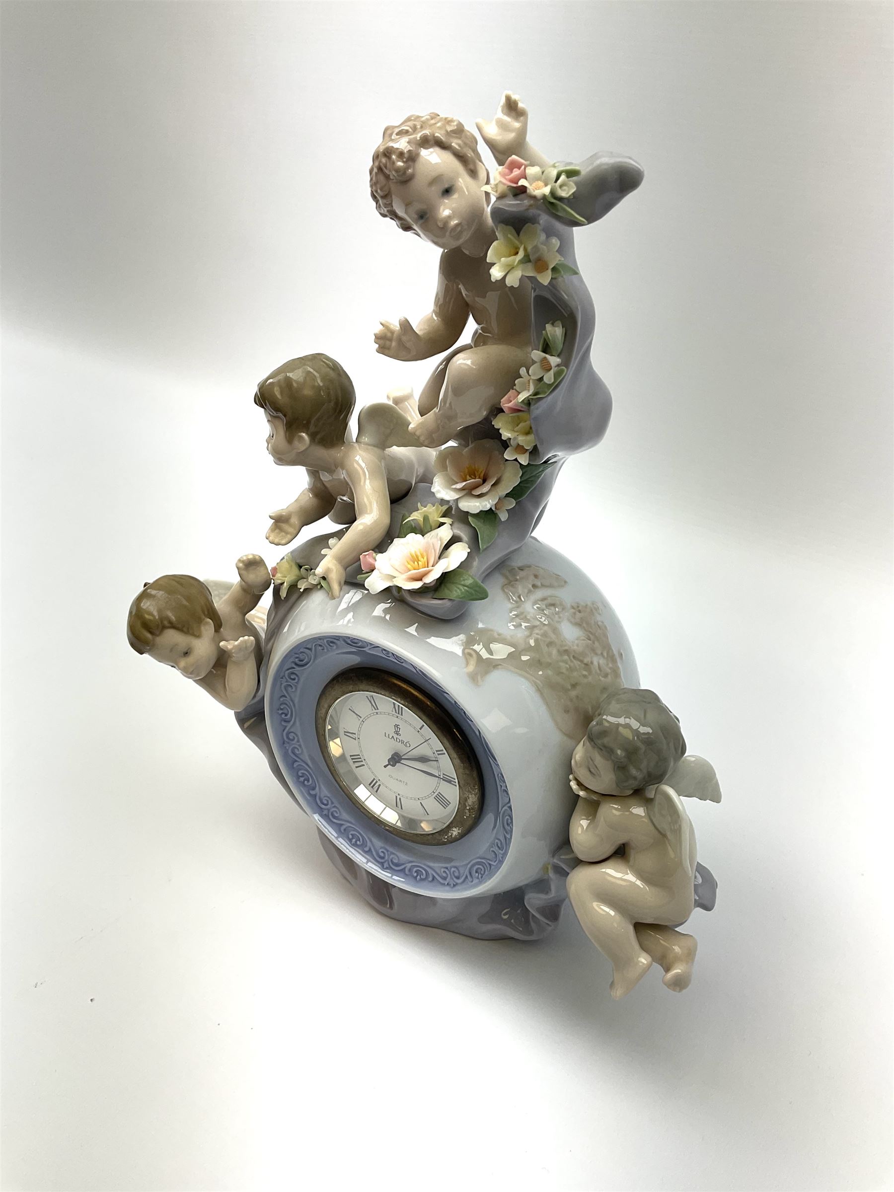 A Lladro mantel clock modelled as a globe with inset clock, surmounted by four putti and floral garlands, with blue printed mark and impressed 5973 beneath, H29cm.