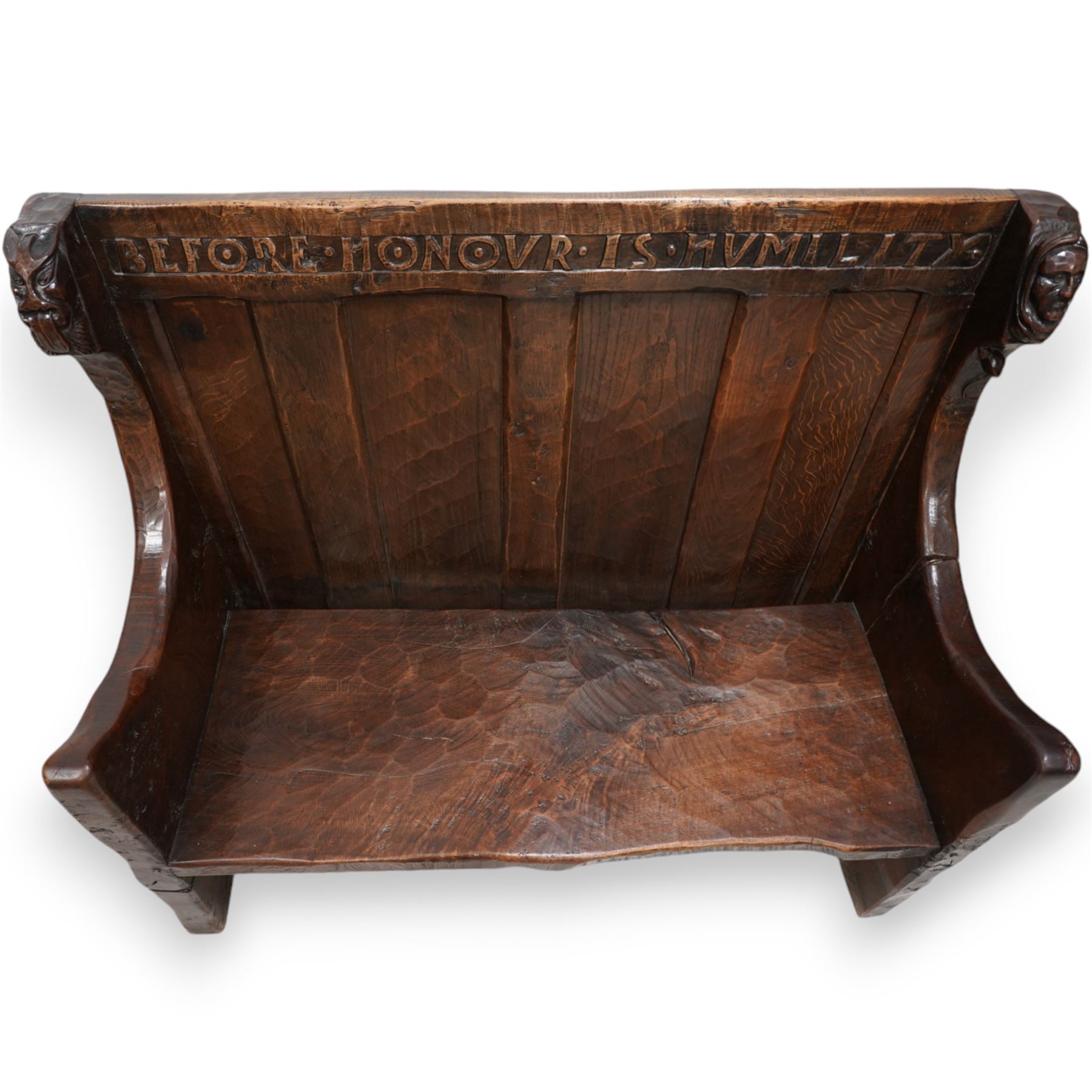 Mouseman - circa. 1920s adzed oak settle or bench, the cresting rail carved with inscription 'Before Honour is Humility', four panel back and plank seat on shaped end supports carved with grotesque masks terminals, carved with mouse signature, by Robert Thompson of Kilburn 
