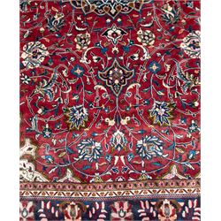 Northwestern Persian Lillihan hand-knotted carpet, madder red field with scrolling vines, rosettes, and palmettes around a central circular medallion in navy, ivory and ochre, and ivory ground spandrels within a navy border of stylized flowerheads and vines between multiple guard stripes 