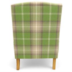 Contemporary green tartan upholstered wingback armchair, with scroll arms and loose seat cushion, raised on turned beech front supports with brass castors
