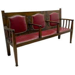 Early 20th century Arts & Crafts oak three-seat settle, upholstered in red leather with stud work, carved with Tulip flowers and scrolled foliage, on square tapering supports with spade feet