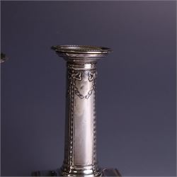 Pair of late Victorian silver mounted candlesticks, the stems embossed with classical ribbon and swag design, upon weighted stepped square bases, hallmarked London 1899, maker's mark worn and indistinct, H12cm