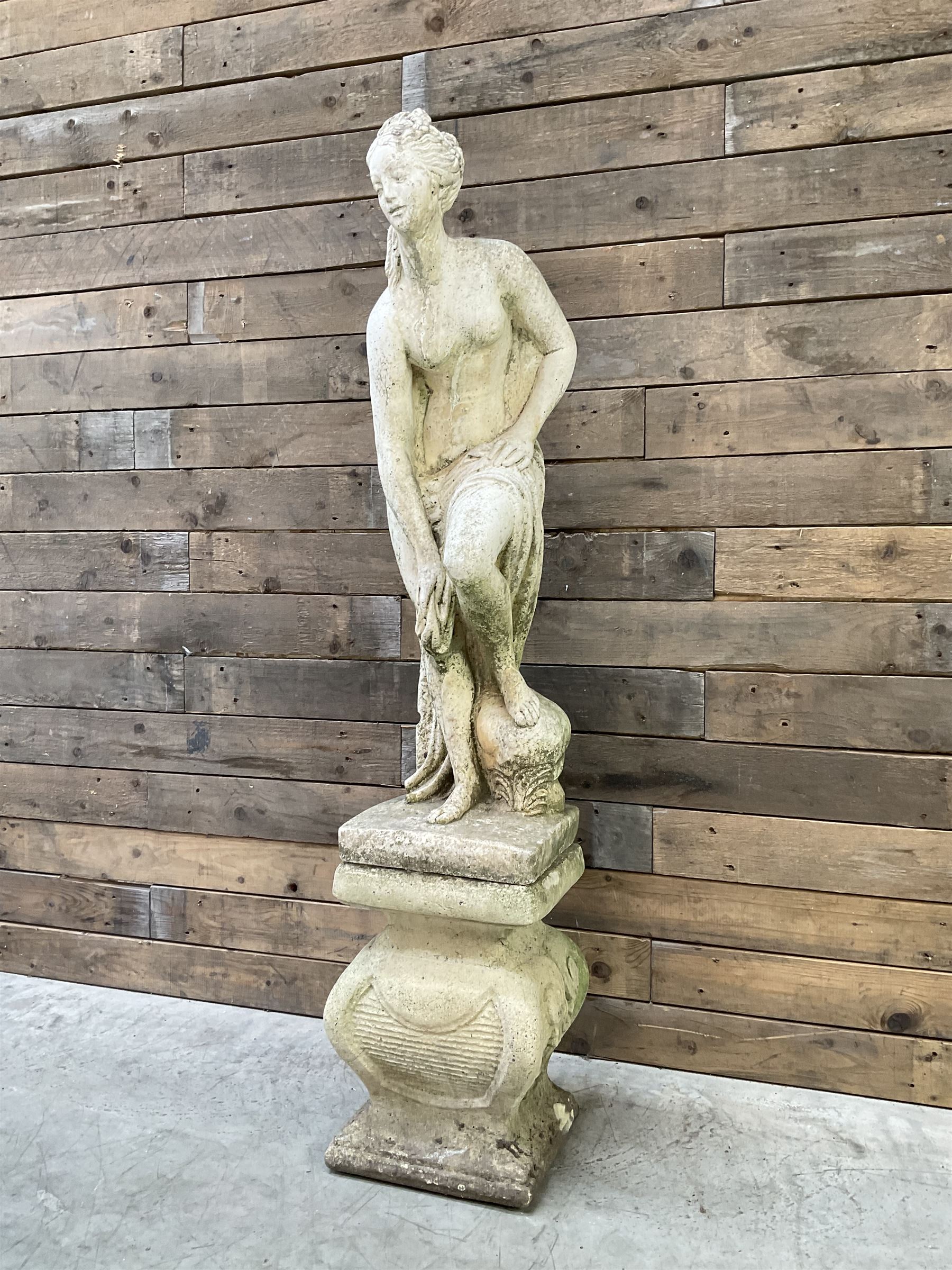 Cast stone garden statue of partially draped classical female figure on ornate pedestal 