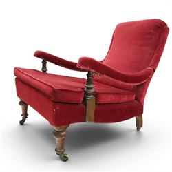 Victorian walnut framed reading open armchair of reclined position, the high sprung back and deep seat upholstered in crimson fabric with matching loose seat cushion, turned arm terminals over turned feet terminating to brass castors