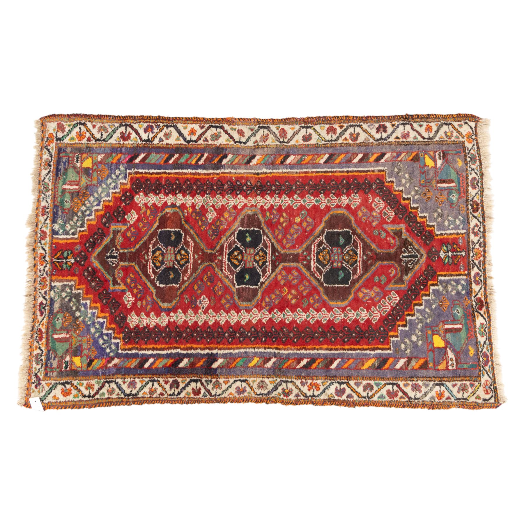 Northwestern Persian village rug, madder red field, with serrated central panel enclosing three linked lozenge medallions, polychromed spandrels, ivory border, and geometric guard stripes  