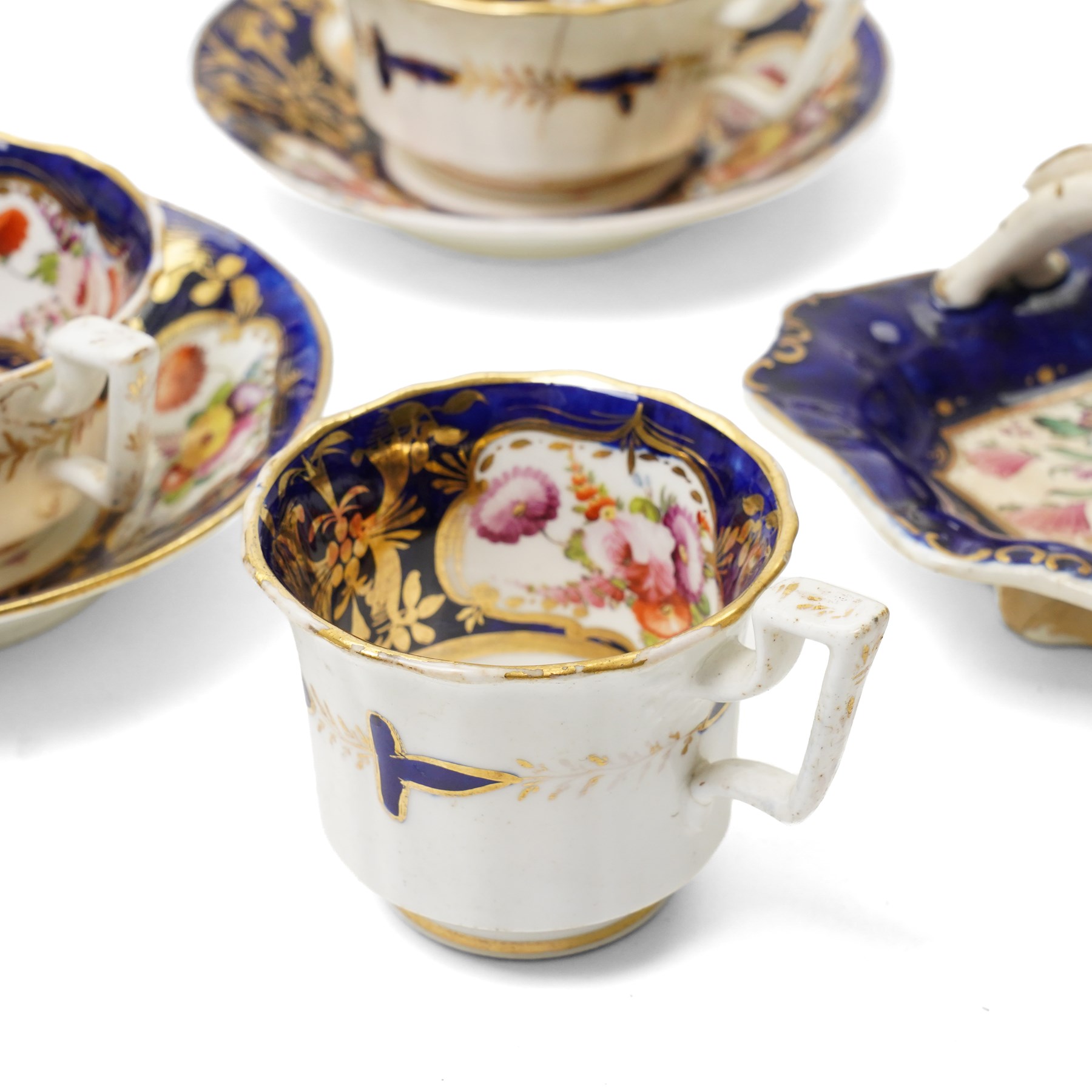 Collection of early 19th century Coalport pattern tea ware decorated with panels of flowers within a blue and gilt surround comprising eight tea cups, three coffee cups, eight saucers, four large plates, two handled sucrier and cover, milk jug and slop bowl and a similar small dish with loop handle
