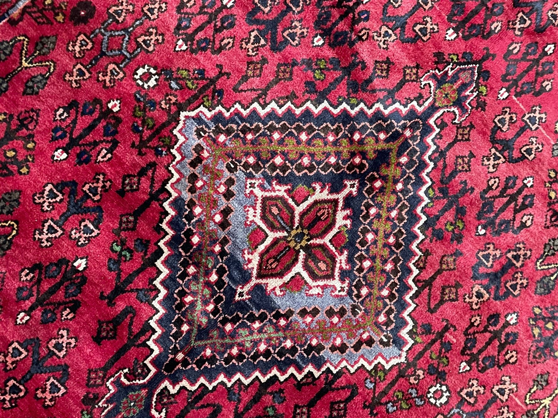 Persian Joshaghan crimson ground rug, stepped lozenge medallion surrounded by repeating foliate lozenge motifs, the border decorated with stylised plant motifs, within geometric guard stripes 