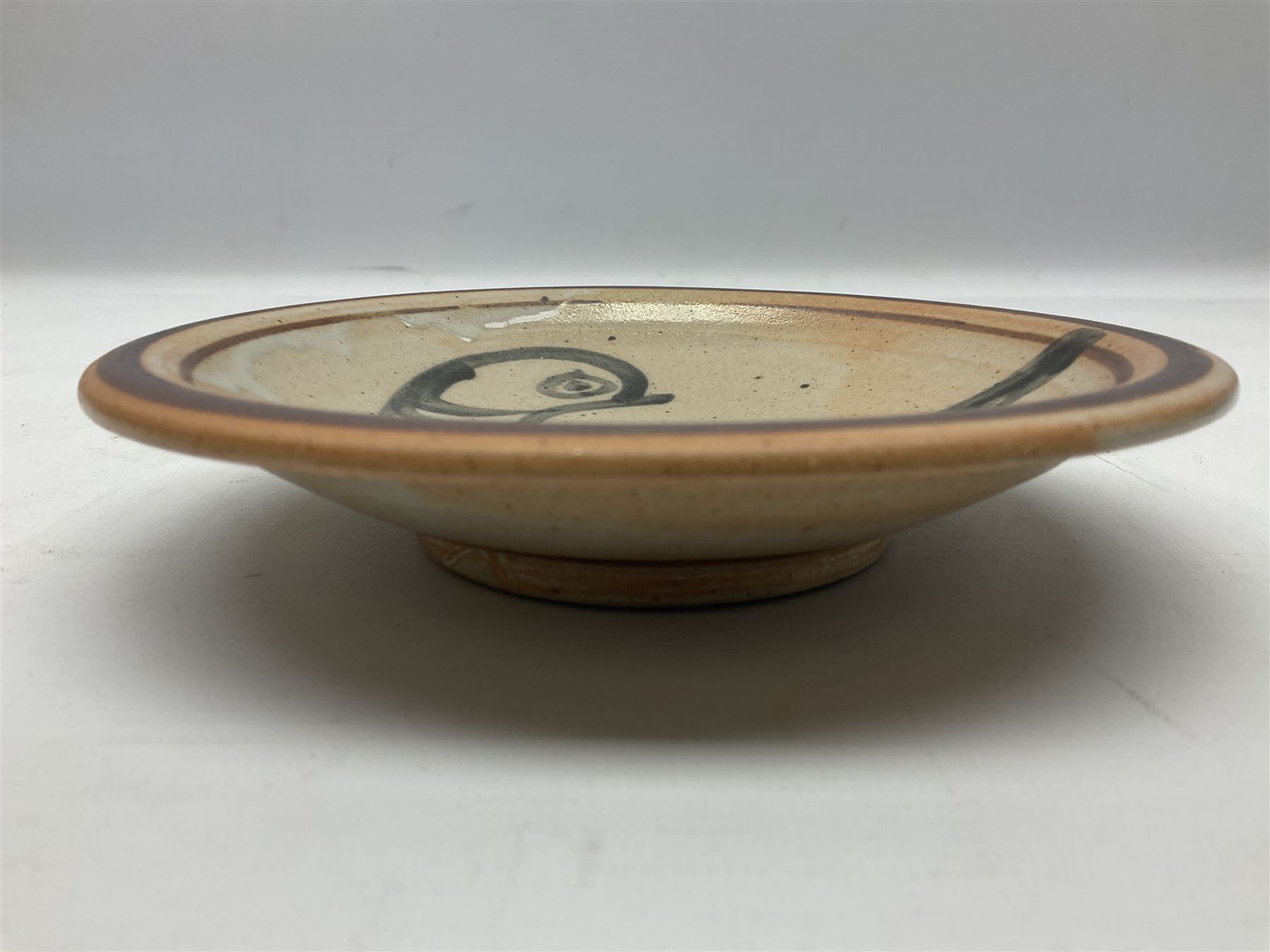 Studio pottery bowl, probably by Svend Bayer of Wenford Bridge, the stoneware body of shallow circular footed form with brushwork decoration of a stylised bird figure in grey upon peach ground within bands of iron red, unmarked, D18.5cm